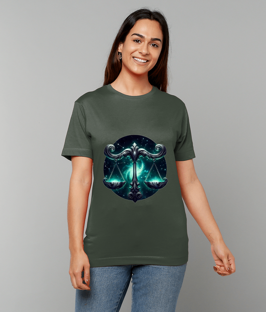 Green T-shirt displays ornate metallic scales emblem over a cosmic teal background, worn by a smiling person standing with relaxed arms against a neutral gray studio backdrop.