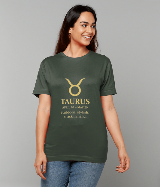 Green T-shirt displays a gold Taurus symbol and text "TAURUS APRIL 20 - MAY 20 Stubborn, stylish, snack in hand." worn by a smiling woman looking right against a plain light-gray studio backdrop.