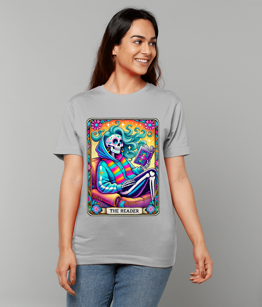 A colorful tarot-style skeleton figure reads a book while lounging on a chair, printed as a large graphic on a gray T-shirt, text at bottom reads THE READER.