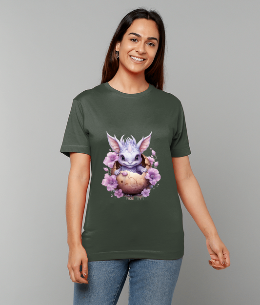 T-shirt shows a small lavender dragon hatching from a cracked egg surrounded by pink flowers worn by a smiling woman against a plain light gray background.