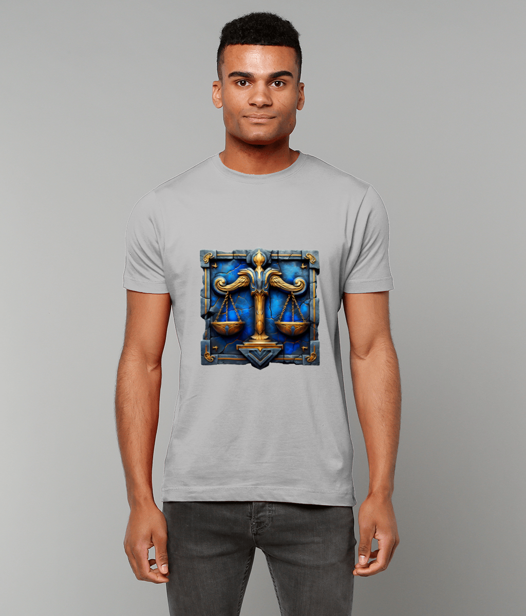 An ornate golden scales emblem centered on a light gray T-shirt, depicting balanced pans over a blue jeweled background; worn by a standing person against a plain neutral backdrop.