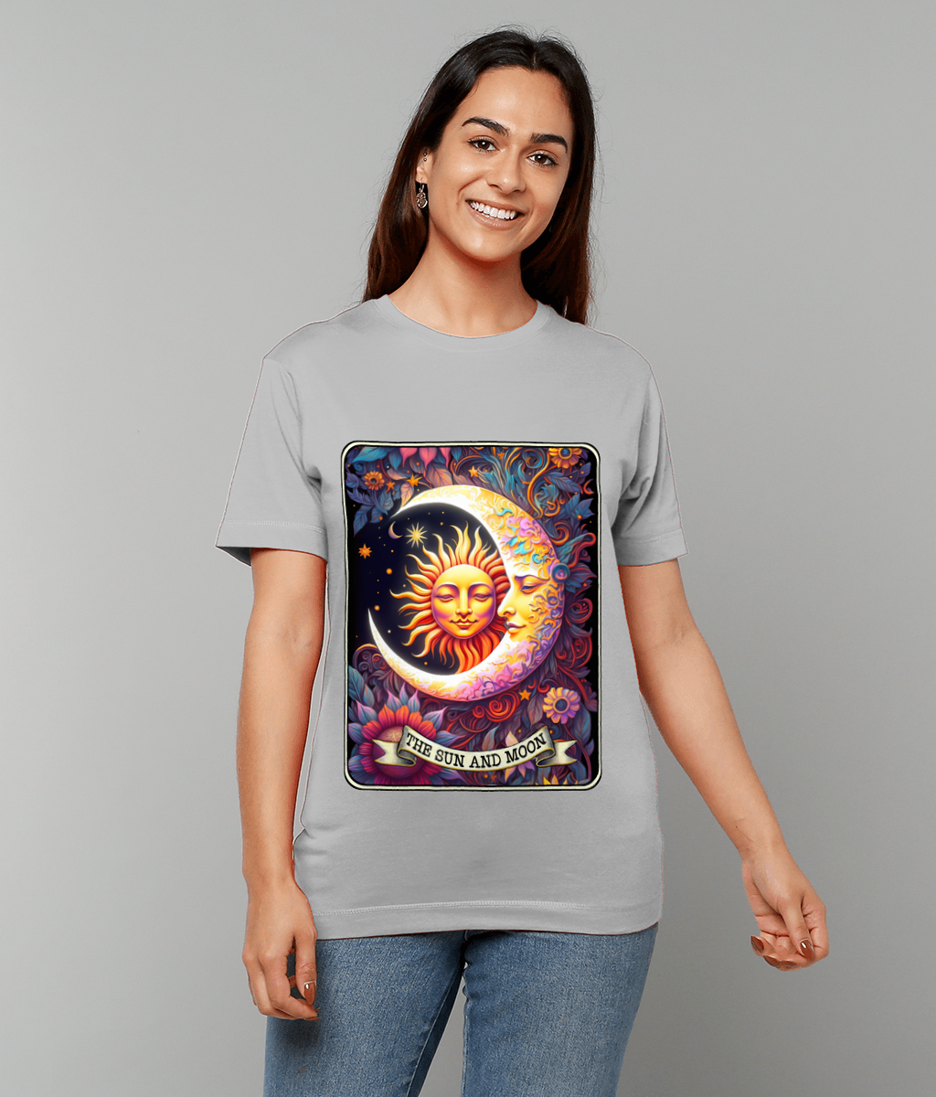 A colorful sun and moon illustration labeled "THE SUN AND MOON" depicts a radiant sun face cradled by a crescent moon face amid stars and floral swirls on a gray T-shirt worn by a smiling person against a neutral background.