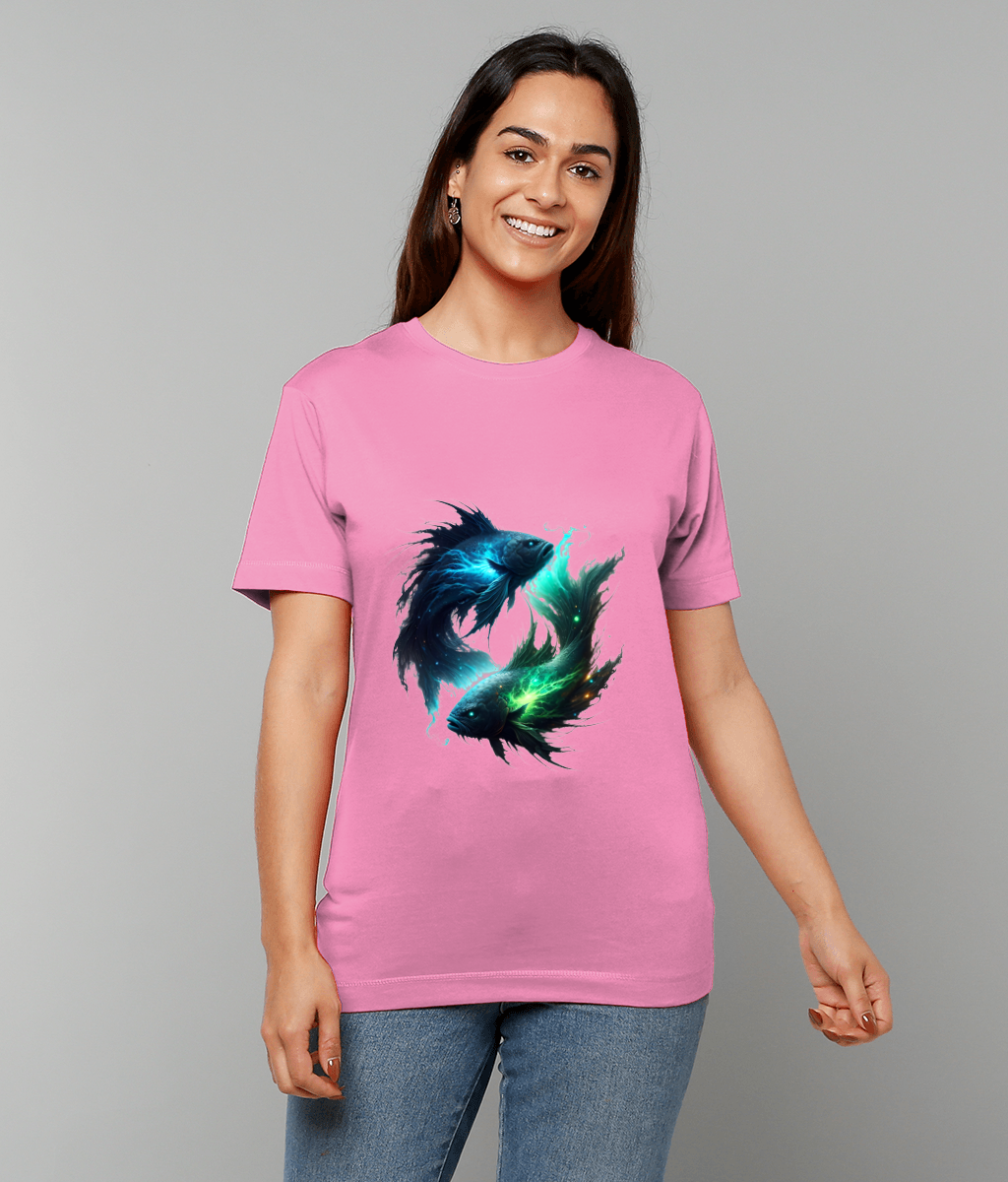Person wearing a pink T-shirt displaying two luminous, stylized fish circling each other while smiling and standing against a plain gray background with blue jeans visible.