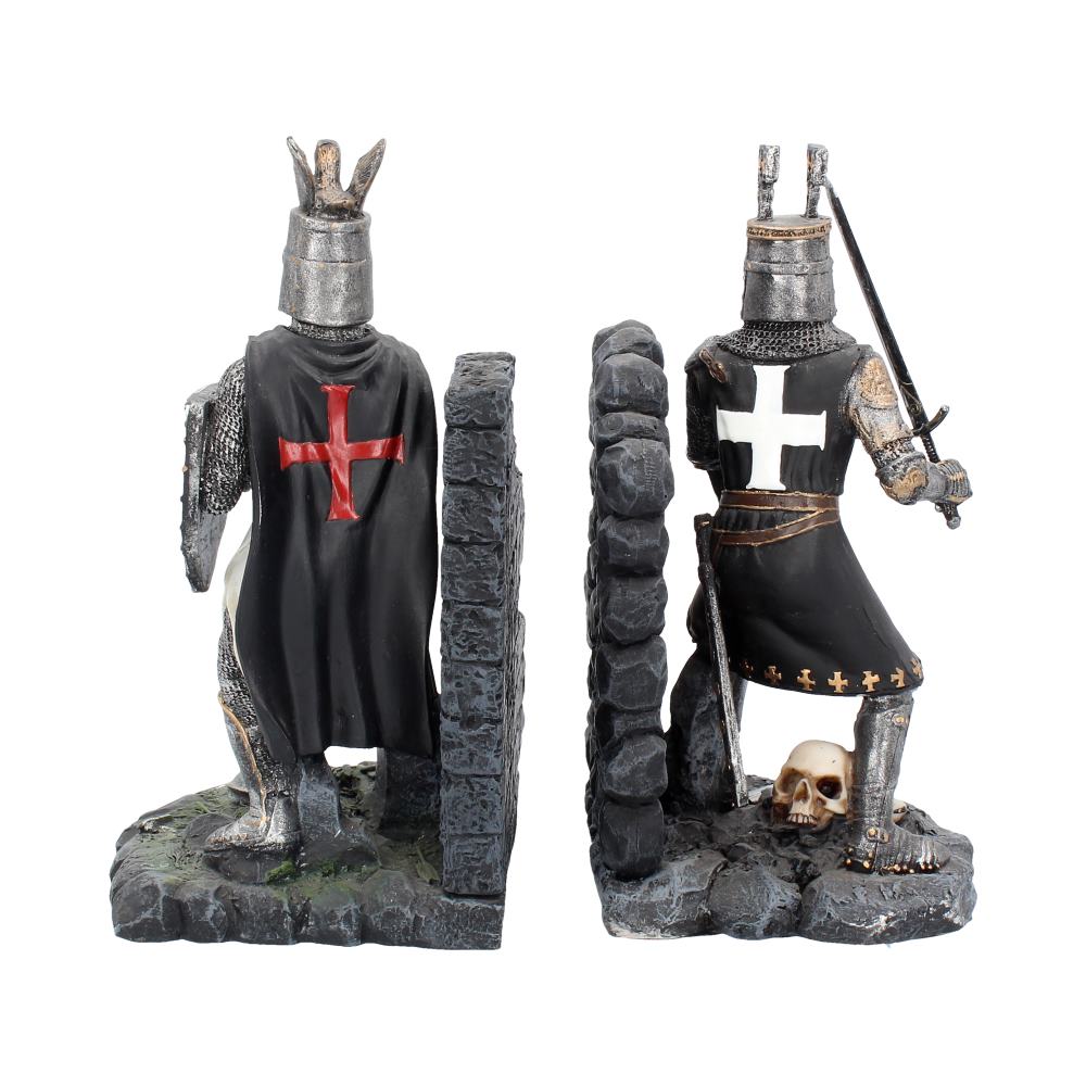 Two medieval knight figurines face each other, separated by a stone wall. One wears a red cross and the other a white cross, both in a rocky, skull-littered setting.