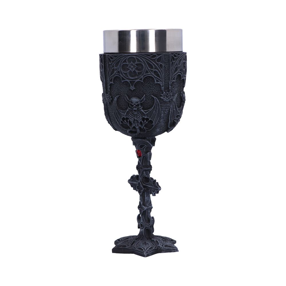 A gothic chalice, etched with bats and floral patterns, stands upright on a white surface. Its stem features decorative crosses with a red jewel accent. The cup is stainless steel.