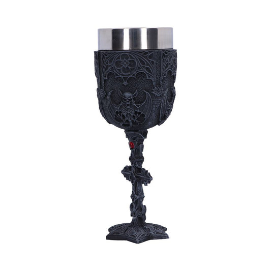 A gothic chalice, etched with bats and floral patterns, stands upright on a white surface. Its stem features decorative crosses with a red jewel accent. The cup is stainless steel.