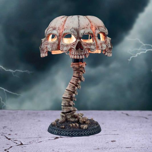 A lamp shaped like a skull cluster rests on a base resembling vertebrae, glowing warmly. It stands on a cracked surface with a stormy sky and lightning in the background.