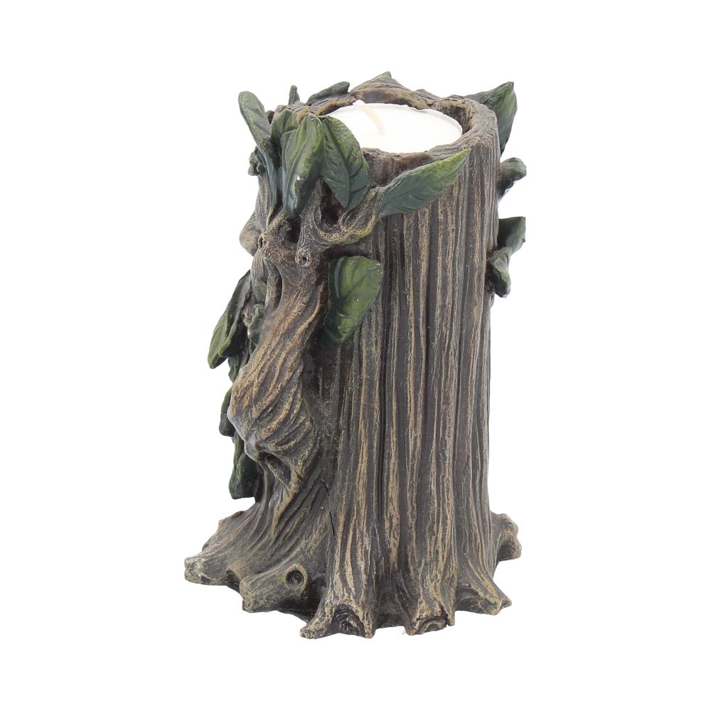A decorative tree stump-shaped candle holder has a small white candle resting within its top, surrounded by green leaves and a face carved into the trunk's side.