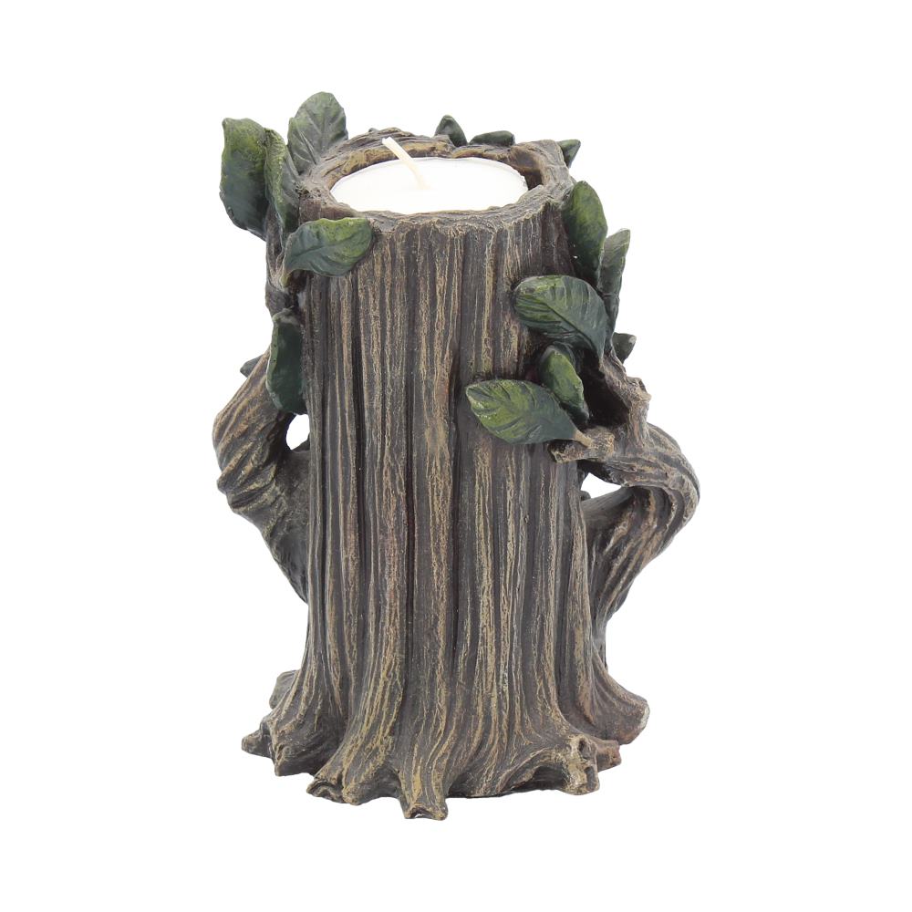 The tree trunk-shaped candle holder holds a small, white, lit candle, surrounded by leaves and small branches on a white surface.