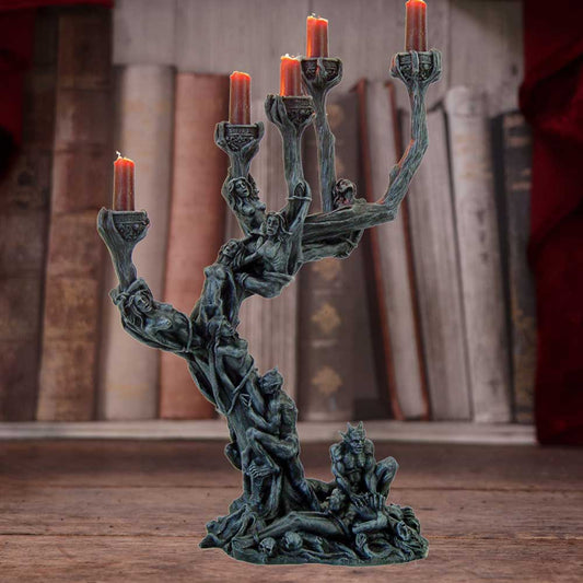 Bronze-toned sculpted candelabra shaped like a twisted tree of entwined human figures holding five lit red candles on a wooden table with blurred old books behind it.