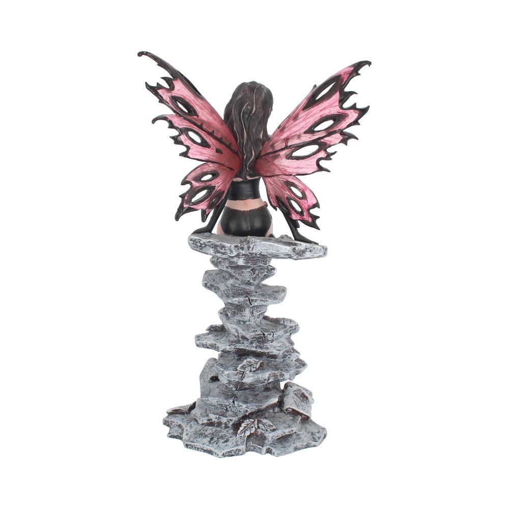 A fairy figurine, with pink and black wings, sits on a gray, stacked-stone column, facing away. The background is plain white.