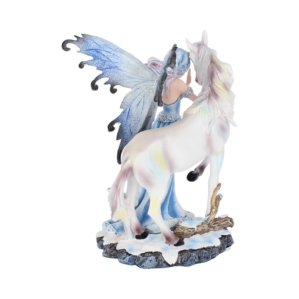 A winged fairy in a long blue dress stands, hand on a white unicorn's face. They are both on a rocky surface covered with snow and small branches.