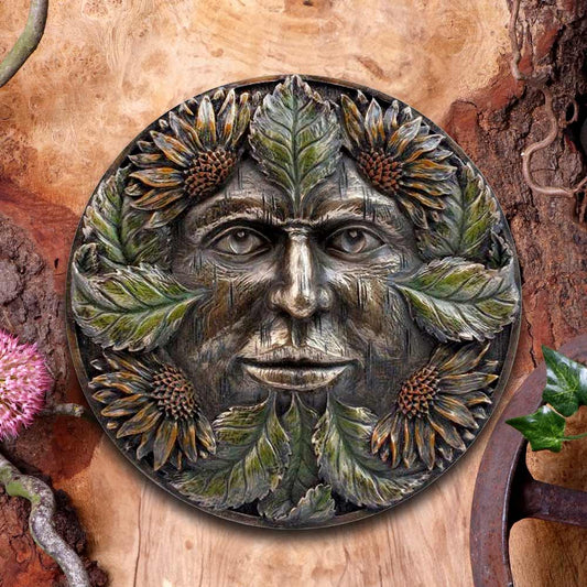 A round, decorative carving features a face intertwined with leaves and sunflowers. It is set against a textured wooden background with scattered flowers and greenery.