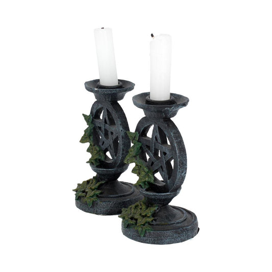 Two ornate dark metal candle holders featuring pentagram cutouts and ivy accents holding partially burned white candles against a plain white background.