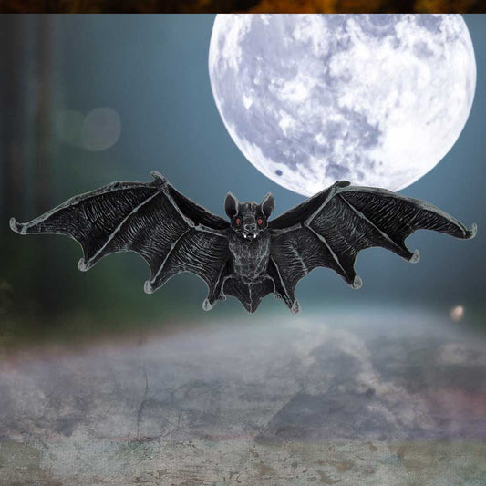 A black bat glides toward the viewer with outstretched wings, mouth open showing tiny fangs, against a bright full moon over a misty roadway at night.