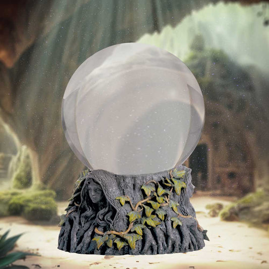 A snow globe with an arboreal base, featuring a hooded face and ivy details, sits in front of a softly blurred fantastical forest backdrop.