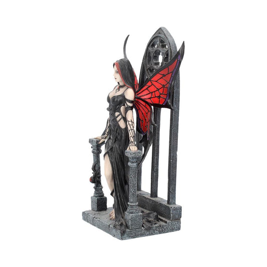 A dark fairy statue stands, leaning against a stone railing, with red and black wings behind her. A gothic window frame sits behind her on a textured base.