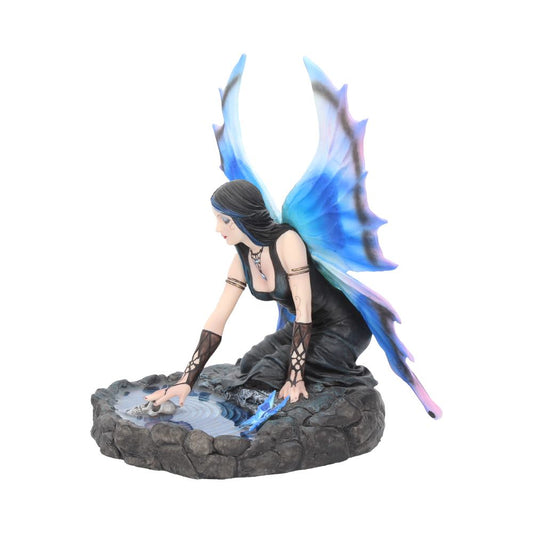 A winged fairy kneels, touching the water of a small rocky pool containing a skull and blue crystal. She is wearing a black dress and has black hair.