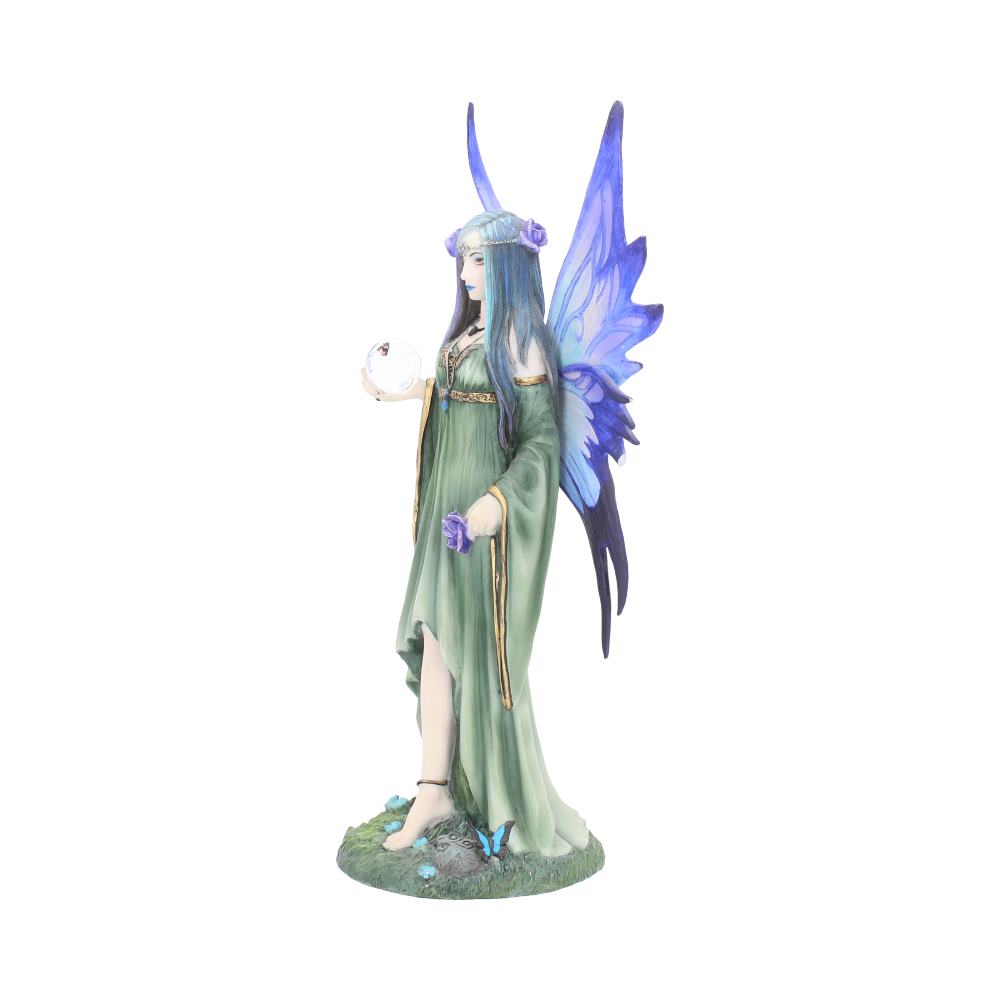 A fairy with blue-purple wings stands, holding a crystal ball in her hand. She wears a green dress and floral headpiece, standing on a grassy base with scattered flowers.