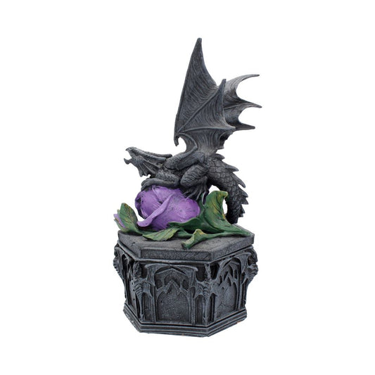 A small, intricately detailed dragon figurine perches atop a decorative, gothic-style pedestal. The dragon is poised over a vibrant purple rose with green leaves.