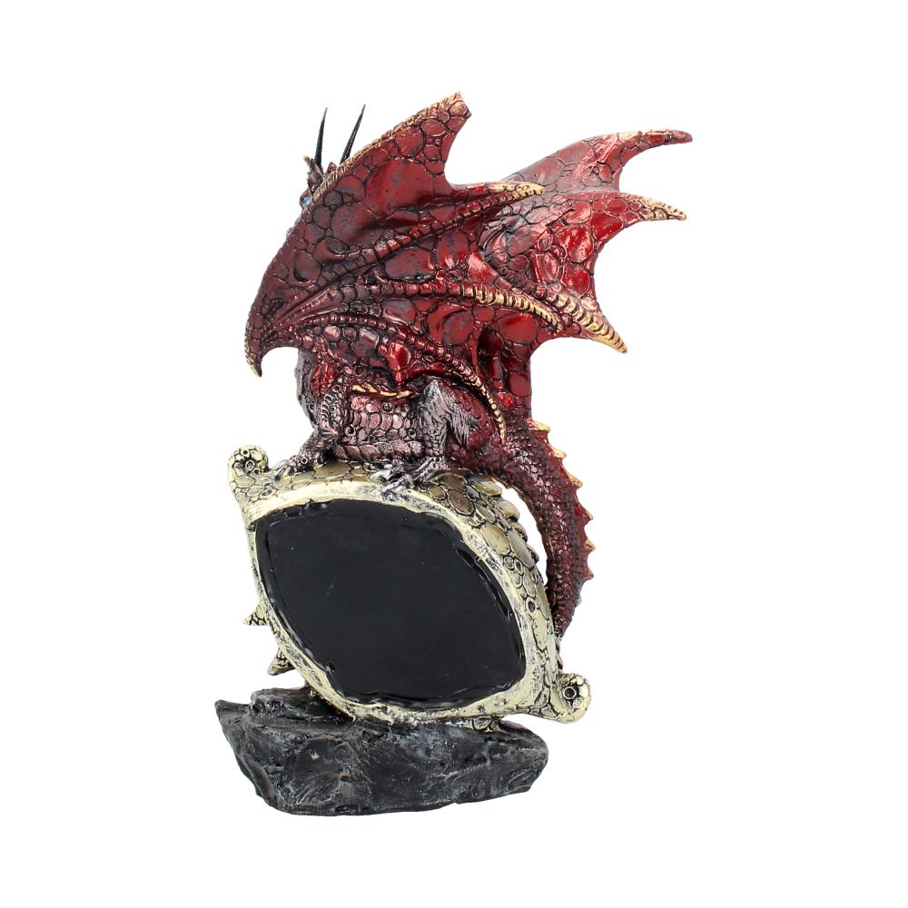 A red dragon figurine perches atop a rugged black rock, encircling a shield-like object with its wings partially spread. The setting is isolated against a plain white background.