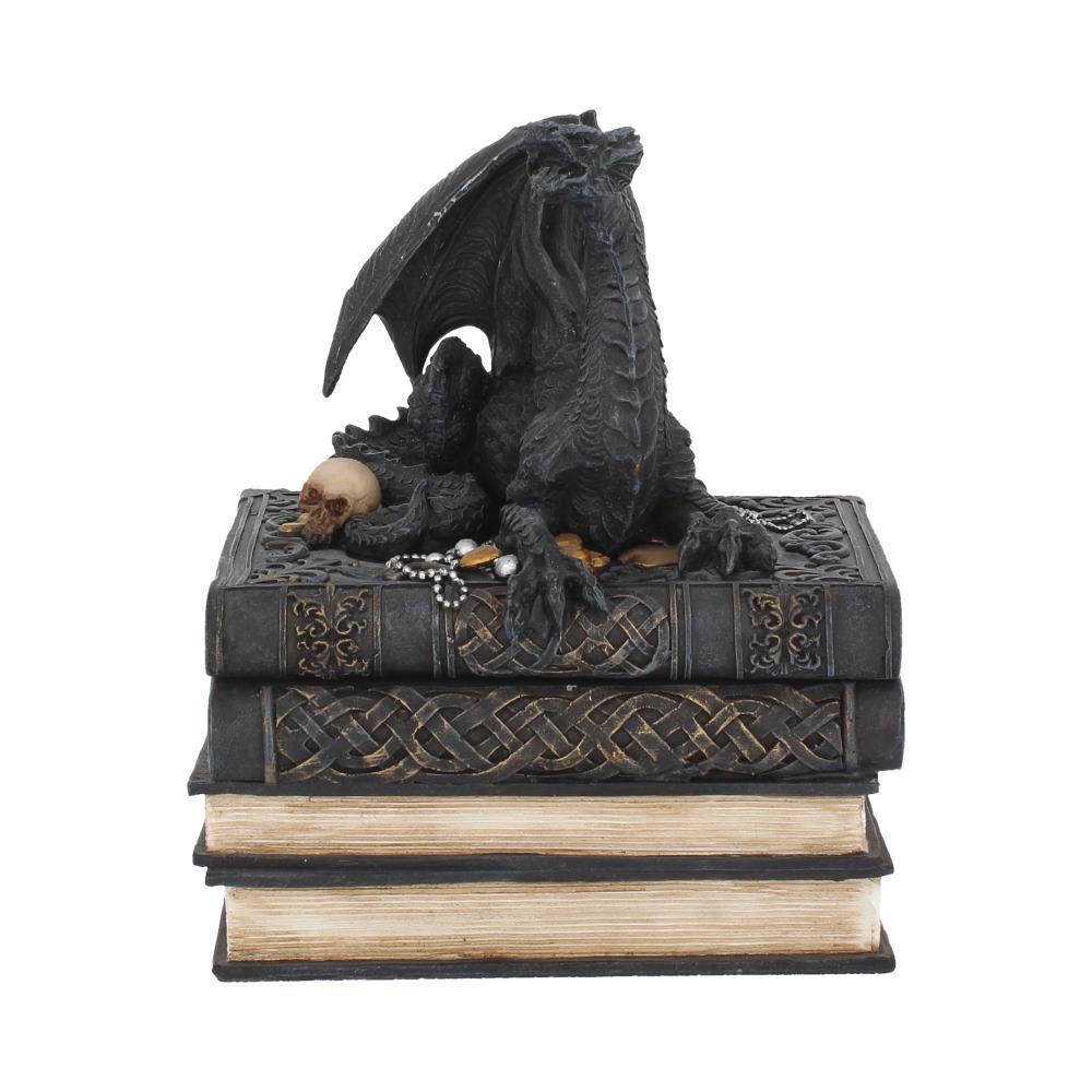 A black dragon figurine rests on intricately designed books, surrounded by small objects like a skull and gemstones in a stacked, mystical setting.