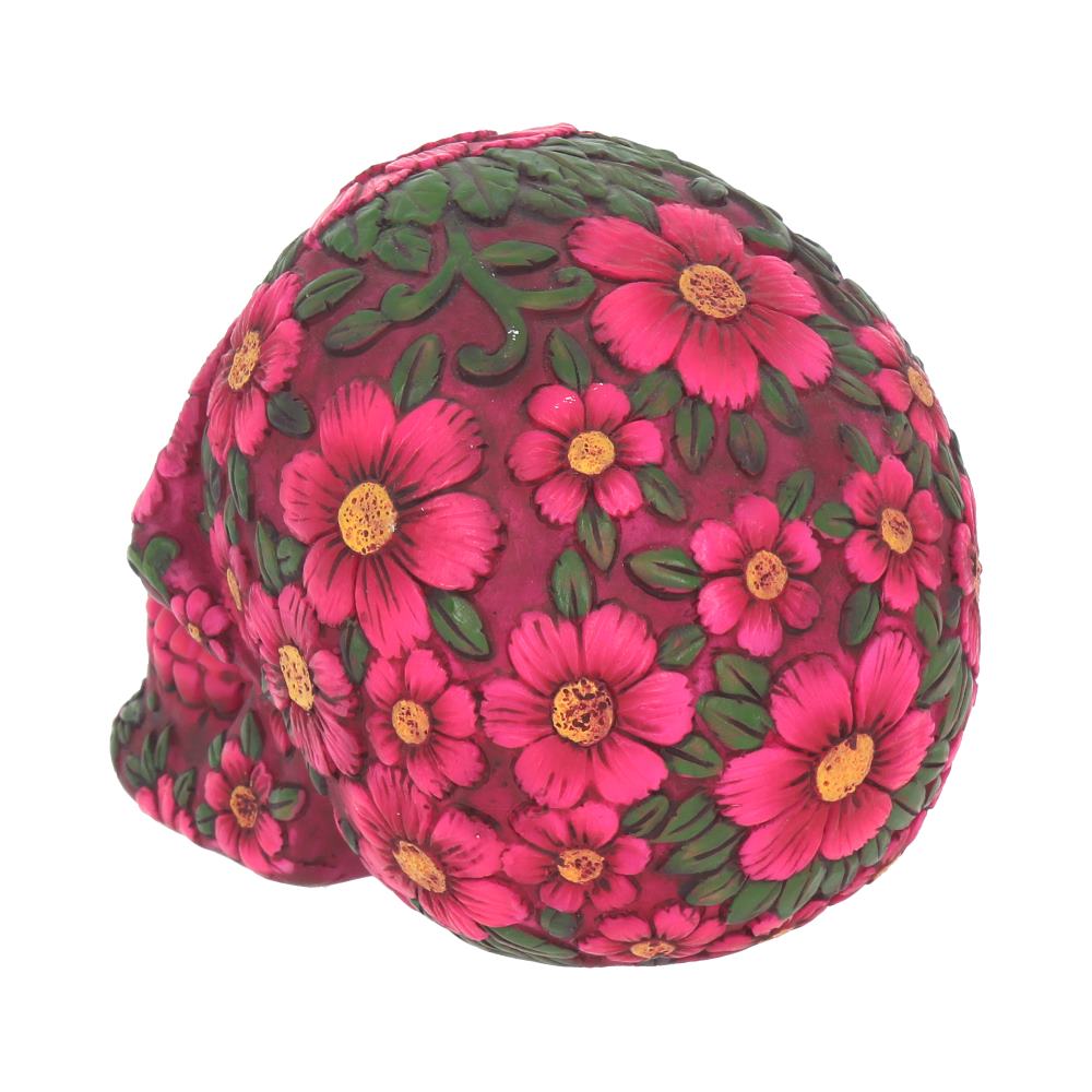 A skull sculpture featuring vibrant pink and yellow flowers with green leaves decorates the surface. It appears against a plain white background, emphasizing the detailed floral pattern.