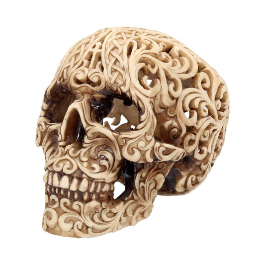 An intricately carved skull features swirling, ornate patterns covering its surface. The design highlights the bone structure, creating a visually striking art piece against a plain, white background.
