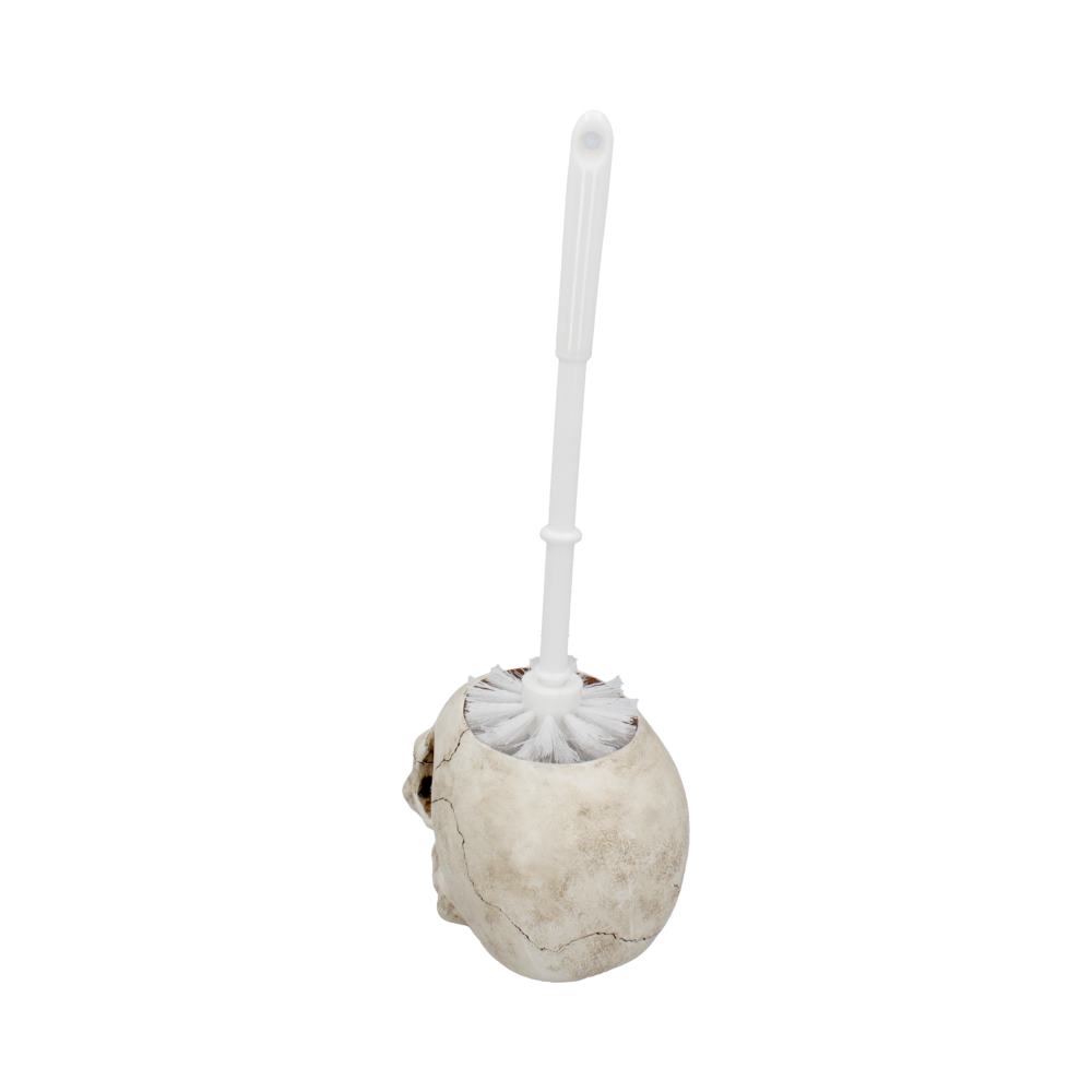 A white toilet brush sits inside a skull-shaped holder, with a cracked, aged appearance, set against a plain white background.