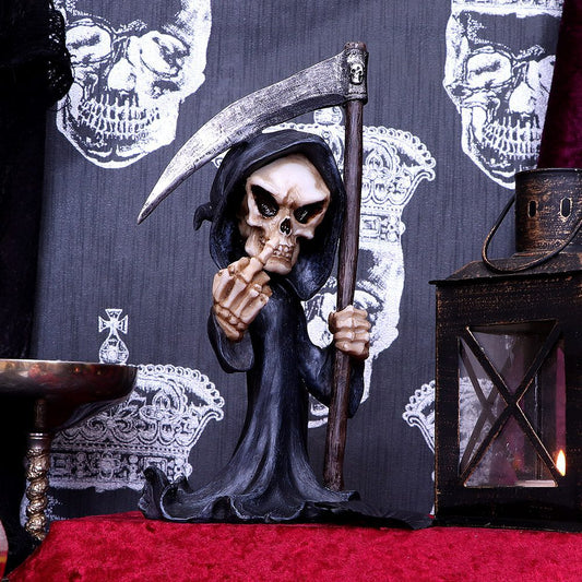 A grim reaper figurine holds a scythe and gestures with its middle finger. It stands on red fabric, surrounded by a lantern and ornate skull-patterned background.