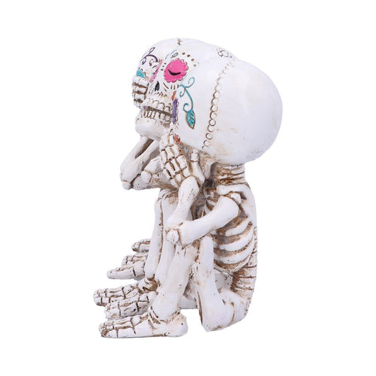 Three decorated skeleton figurines are seated in a row, each covering their eyes, ears, and mouth respectively. They are adorned with colorful floral designs against a plain white background.