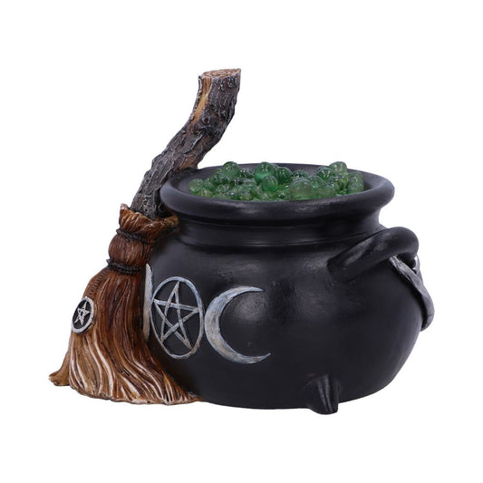 A black cauldron filled with green spheres stands beside a broomstick. The cauldron is adorned with crescent moon and pentacle symbols, evoking a mystical theme on a white background.
