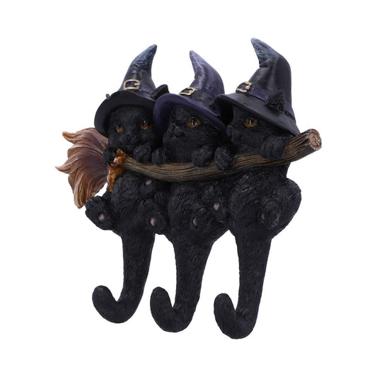 Three black cat statues wear witch hats, perched on a branch. Their bodies form hanging hooks, with a broom leaning on the branch's side against a white backdrop.