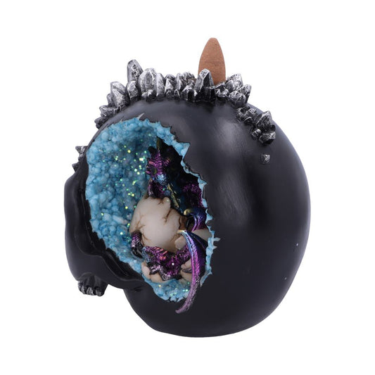 A black, skull-shaped incense burner, adorned with crystals, houses a purple dragon figurine inside a geode-like cavity.  A cone-shaped incense stick rests atop.