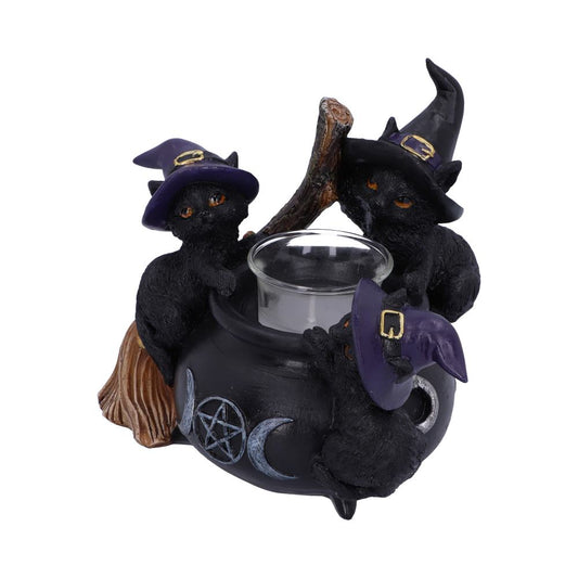 Three black cat figurines wearing witch hats surround a black cauldron with a candle holder insert, and symbols of a pentacle and crescent moons.