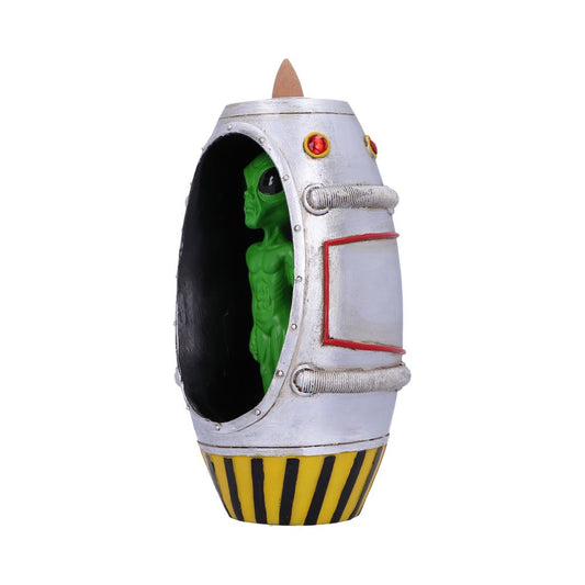 A green alien figurine is contained inside a silver, yellow, and red cylindrical incense burner.  The burner has a pointed top and sits on a white background.