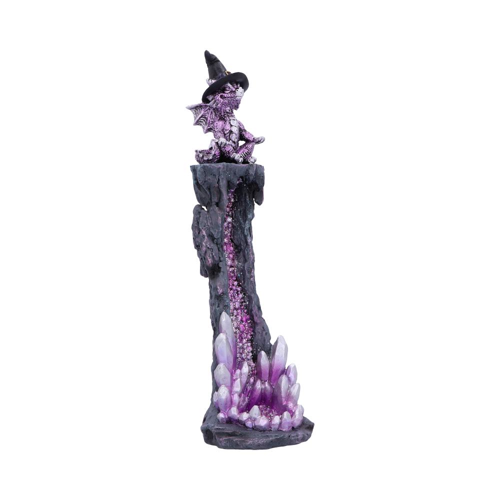 A small dragon figurine, wearing a witch's hat, meditates atop a purple crystal-filled rock formation.