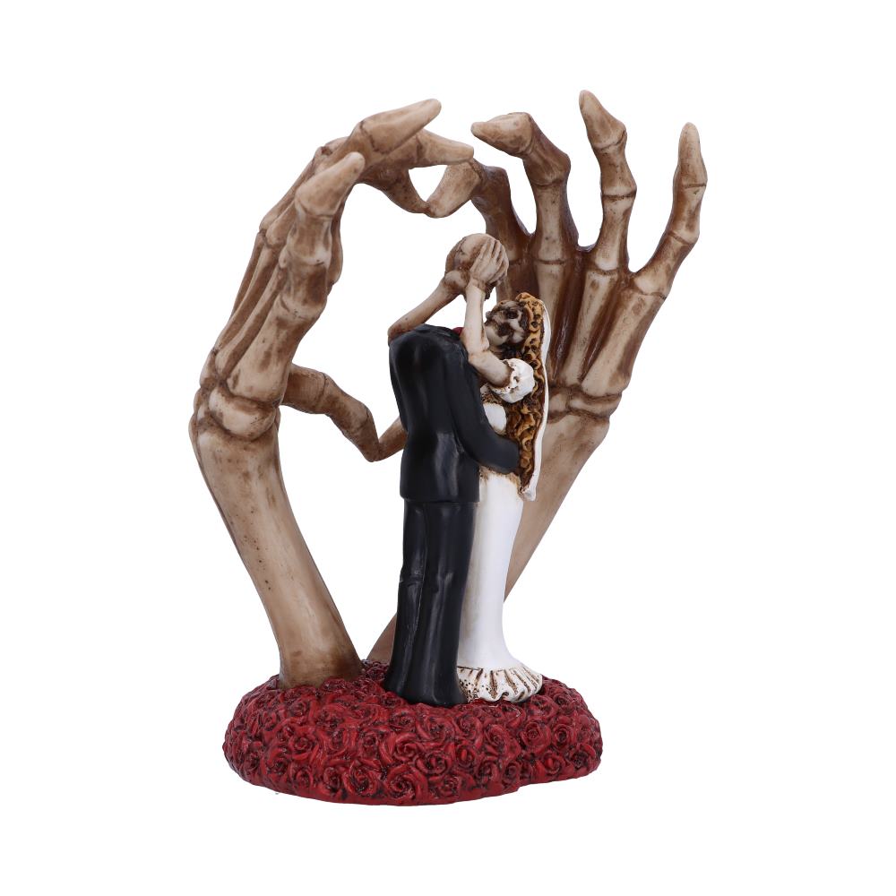 A bride and groom figurine embrace, encircled by large skeletal hands, standing on a base of red roses, symbolizing a mix of romance and macabre themes.