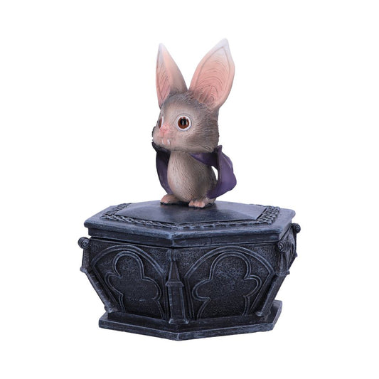 A small bat figurine with large ears and a purple cape sits atop an ornate, black, hexagonal box, resembling a decorative, gothic-style pedestal.