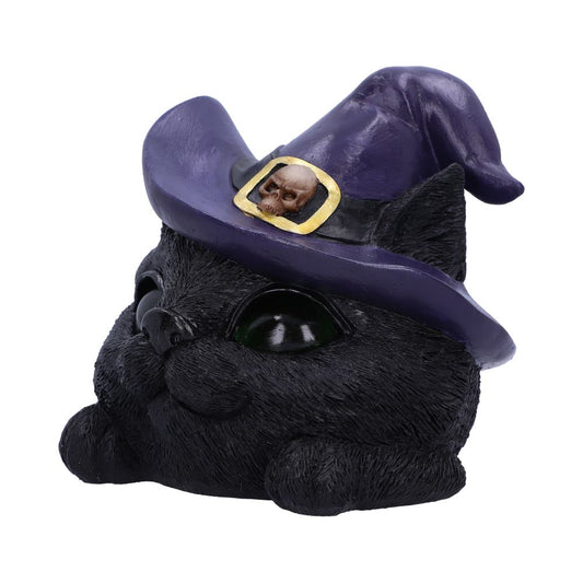 A small black cat figurine wears a purple witch hat adorned with a skull emblem. The cat gazes upward, against a plain white background.