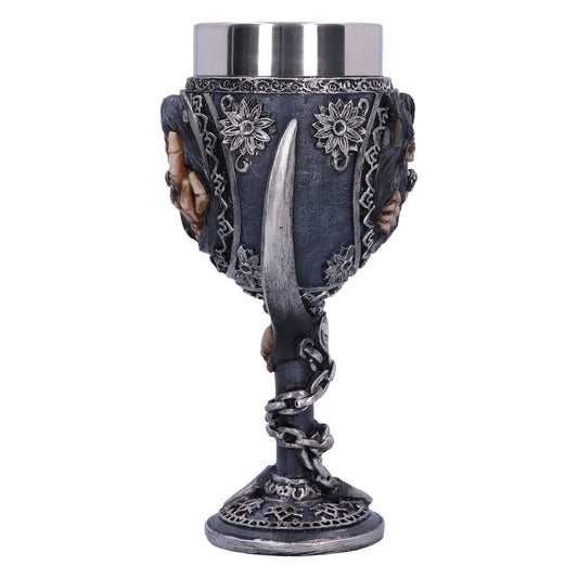 A decorative goblet, silver and dark blue, stands on a white surface. The stem is wrapped with a silver chain, and the cup features skulls and flowers.