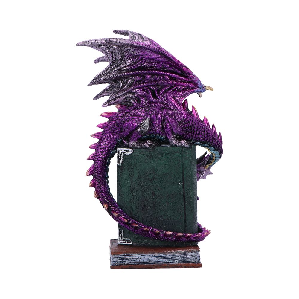 A purple dragon figurine sits perched atop a textured green book, its tail curling around the spine, placed on a wooden base, set against a plain background.