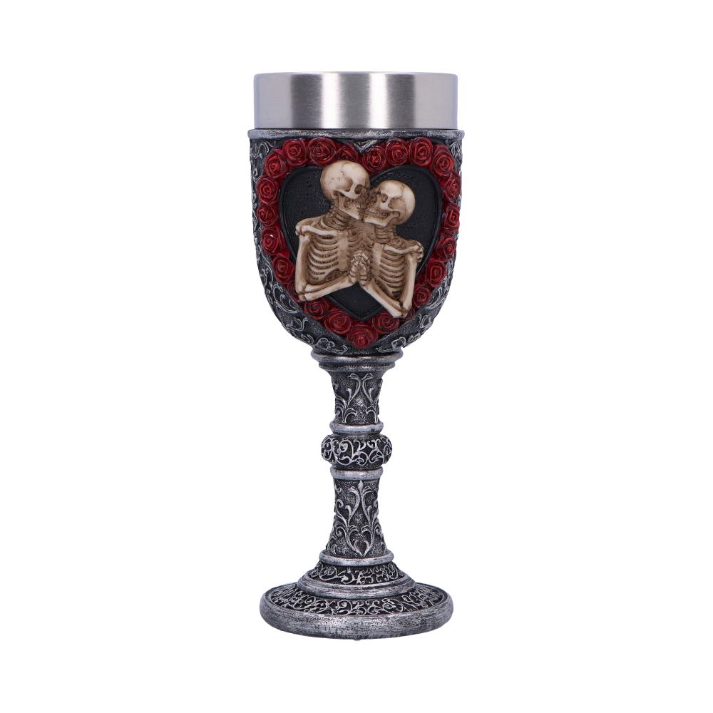 A metal and dark grey goblet displays two skeletons embracing in a heart of red roses on its cup. Its stem and base have ornate designs and it sits in a white space.