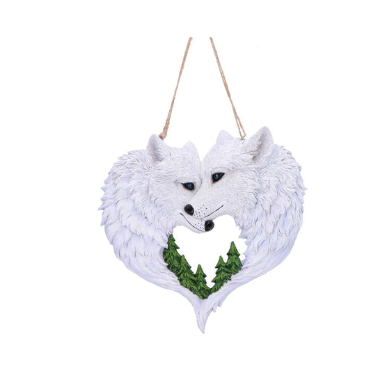 Two white wolf heads form a heart-shaped wreath, their noses touching as they nuzzle, hanging from a twine loop above with three green pine trees visible inside against a white background.