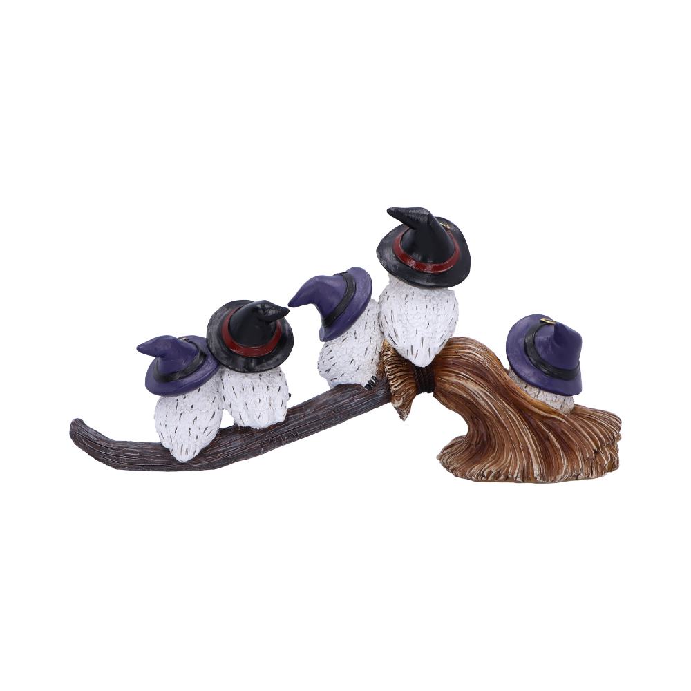 Five small white owls, wearing witch hats, perch on a curved wooden branch and mushroom structure. The hats are black with purple and red accents.
