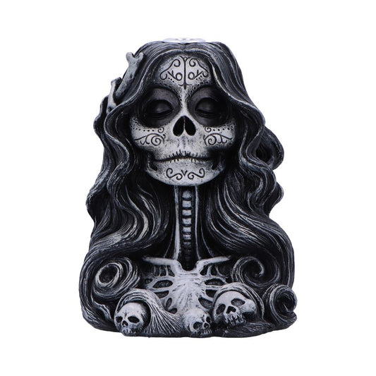 Skull-faced figurine sits facing forward, hair flowing around a visible ribcage and three small skulls at base, decorated with stylized Day of the Dead facial markings on a white background
