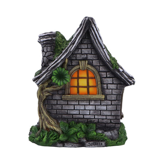 Stone cottage figurine with glowing orange window, vines climbing its textured brick walls, a twisted tree trunk at the front and leafy base, photographed against white background Text: MEXICO