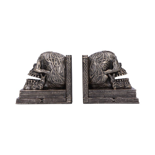 Pair of ornate skull bookends face each other, carved with Celtic knot patterns and aged metallic finish, resting on stacked-book bases against a plain white background.