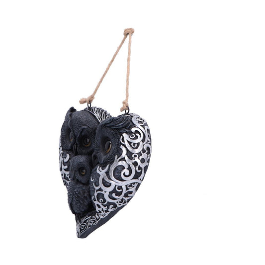 Heart-shaped hanging ornament depicts three carved owls nestled within ornate silver scrollwork, painted black and silver, suspended by a twisted twine loop against a plain white background.