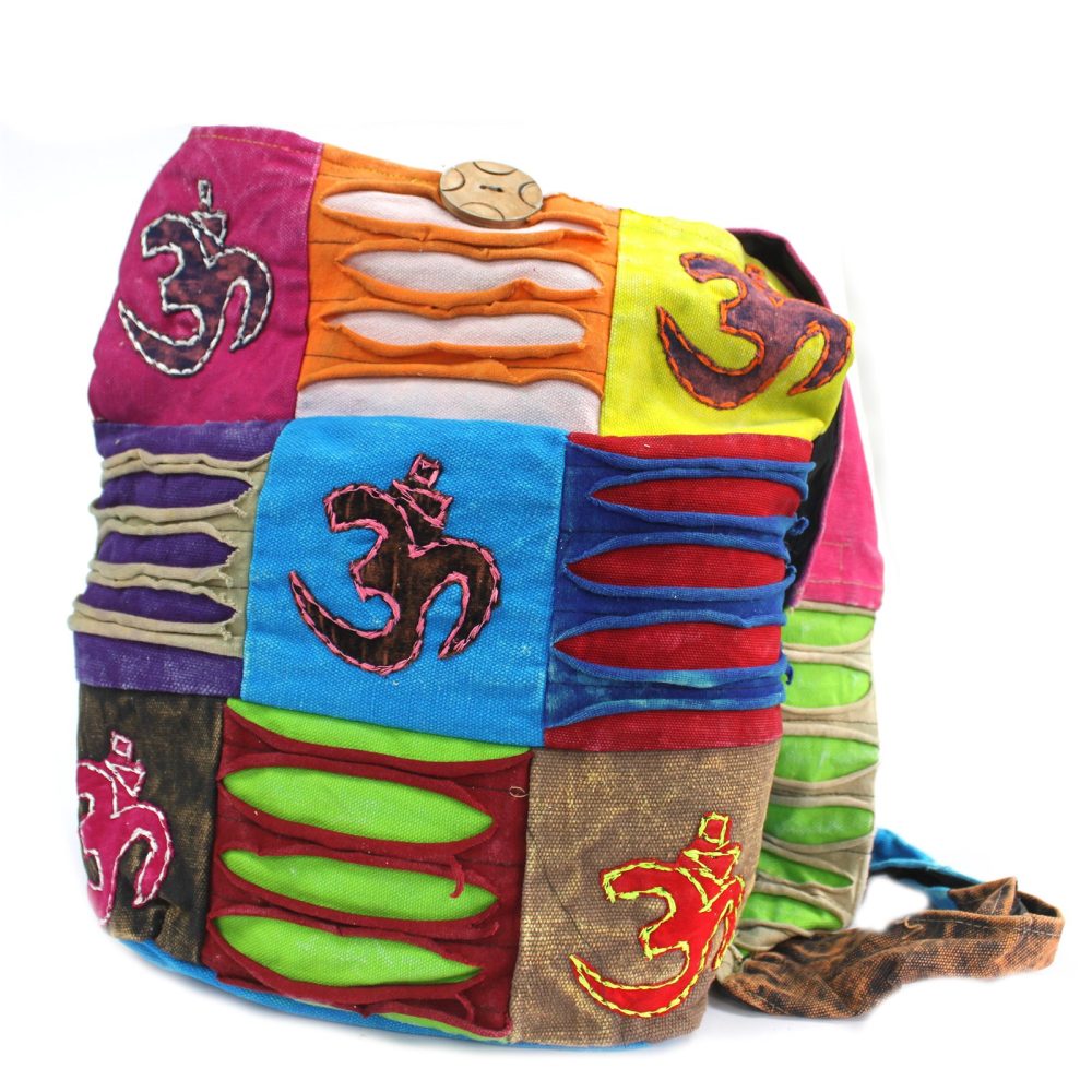 A colorful patchwork bag is displayed against a white background. The bag features Om symbols stitched onto various fabric squares and a wooden button closure at the top.